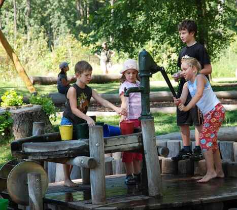 Vier Kinder, die an einem Brunnen auf dem Abenteuer- und Naturspielplatz mit Wasser herumspielen