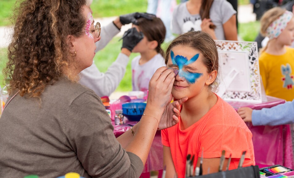 Eine Dame schminkt ein Kind mit bunten Farben im Gesicht beim Kinderschminken