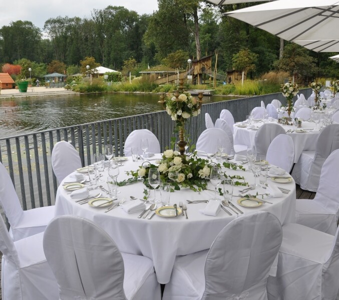 Tables festively laid in white with white roses on the terrace of the restaurant GAUMENWEIDE by the water lily pond