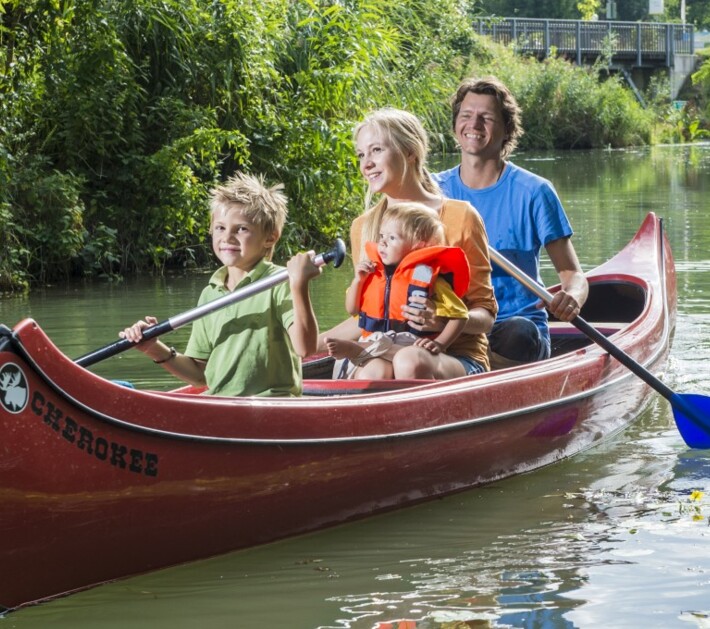 Eine vierköpfige Familie, die mit einem roten Kanu durch die Tullner Donauauen fährt